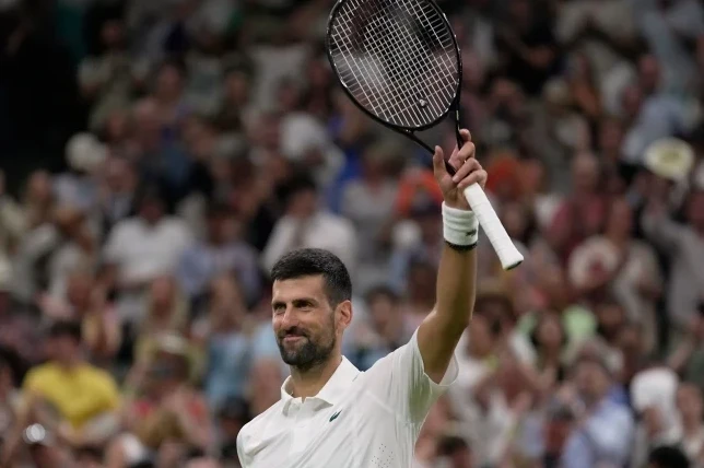 Novak Đoković podiže reket u zrak u znak pobjede, gledajući prema publici na Wimbledonu.