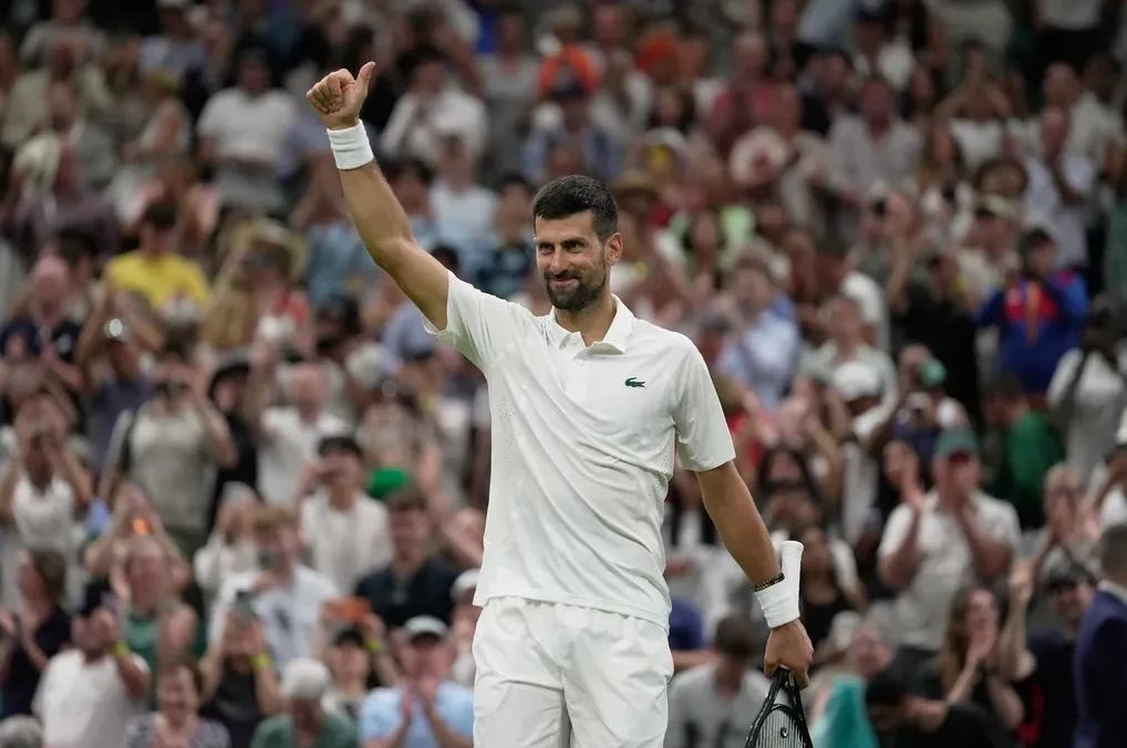 Novak Đoković podiže palac gore dok slavi pobjedu na turniru Wimbledon, okružen publikom.