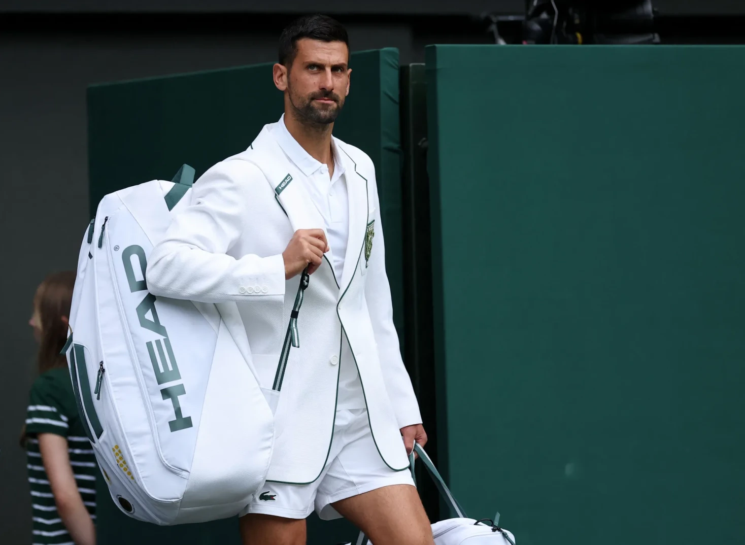 Novak Đoković nosi bijelo odijelo i torbu sa reketima na Wimbledonu