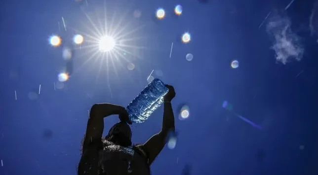 Osoba siluete prska vodu iz plastične boce prema nebu na sunčan dan.