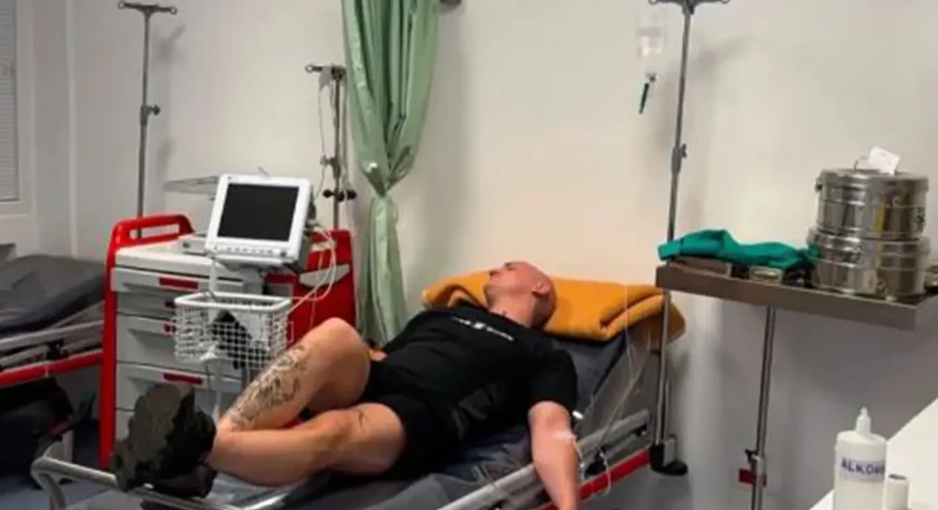 Muškarac leži na bolničkom krevetu u sobi sa medicinskom opremom.