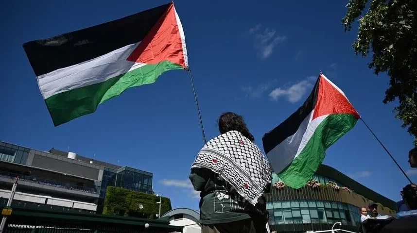Osoba u tradicionalnom palestinskom šalu drži palestinsku zastavu na jarbolu.