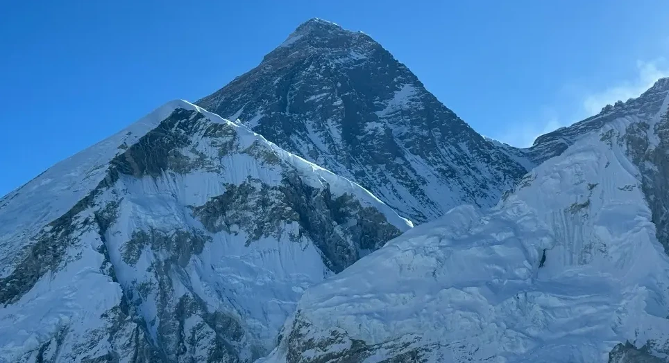 Pogled na snijegom prekriveni vrh planine Everest pod vedrim plavim nebom.