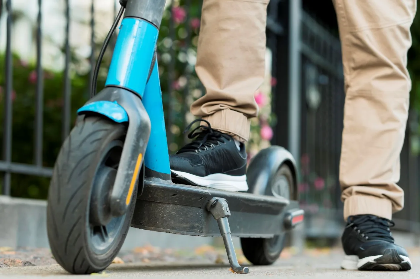 Osoba u bež pantalonama i crnim patikama stoji na plavoj električnoj rolki.