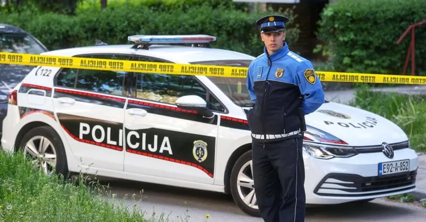 Policijski službenik stoji ispred policijskog automobila sa podignutom trakom za obilježavanje