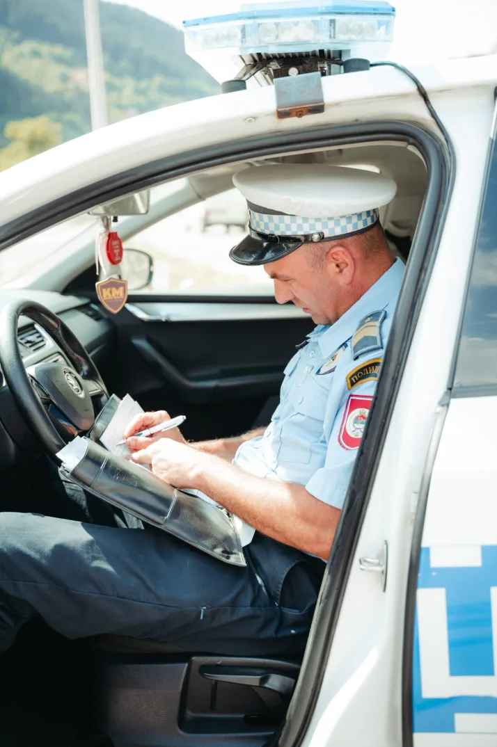 Policajac u uniformi sjedi u automobilu i piše u notes.