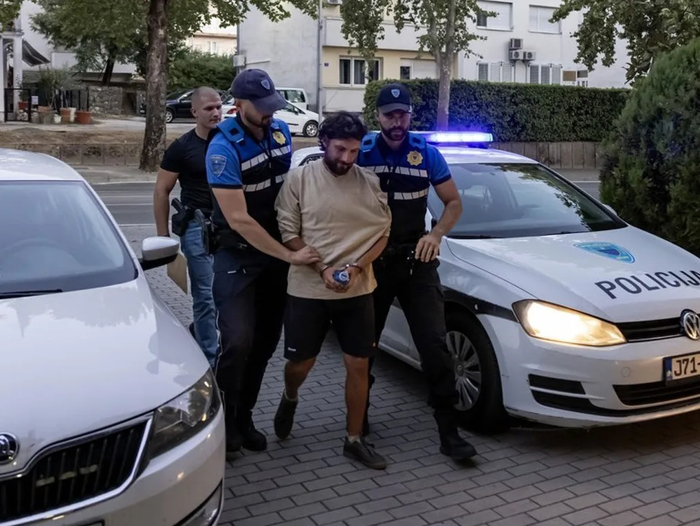 Policajci vrše hapšenje muškarca ispred policijskog vozila.