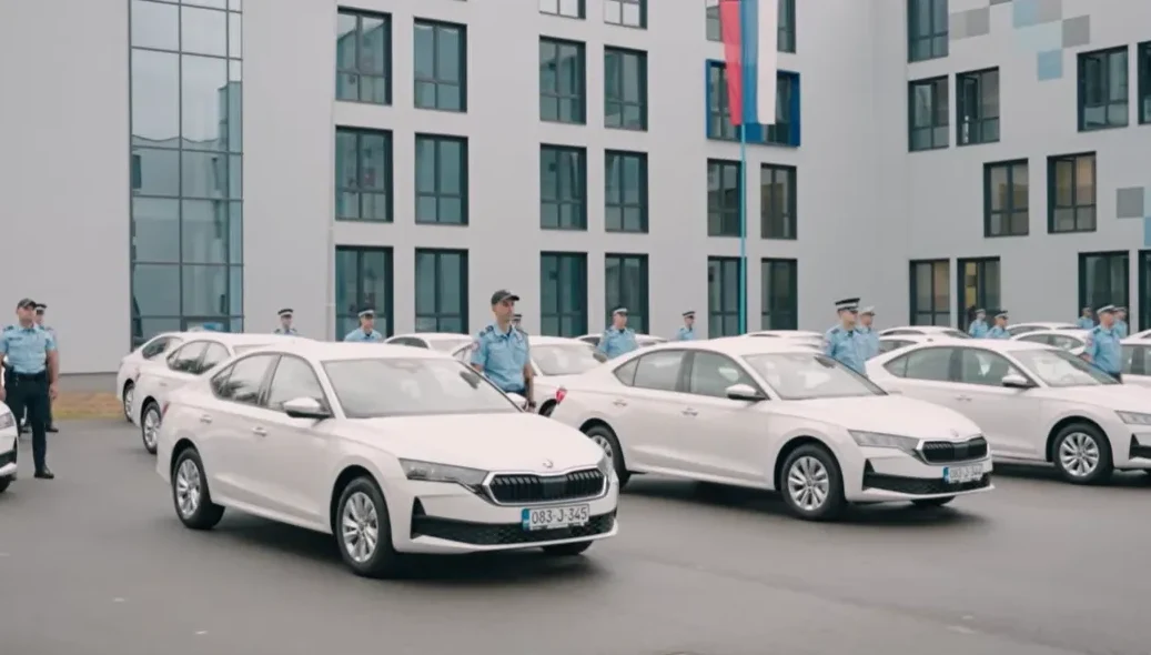 Policajci u uniformama stoje pored novog voznog parka bijelih automobila ispred moderne zgrade.