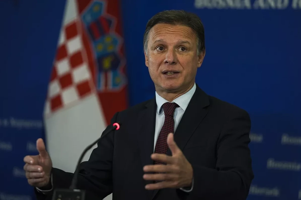 Političar u tamnom odijelu i kravati govori ispred hrvatske zastave.