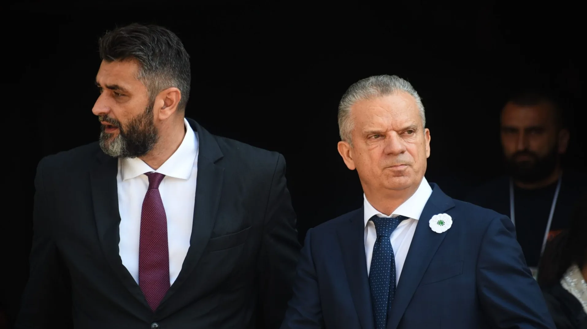 Dva muškarca u odijelima, jedan s tamnom kosom i bradom, drugi s kratkom sijedom kosom.