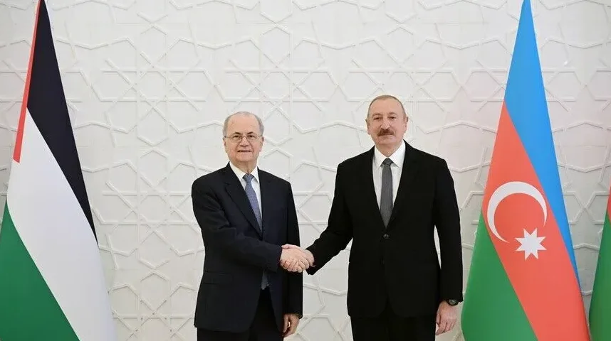 Predsjednik Azerbejdžana Ilham Aliyev i palestinski predstavnik se rukuju ispred zastava dviju zemalja.