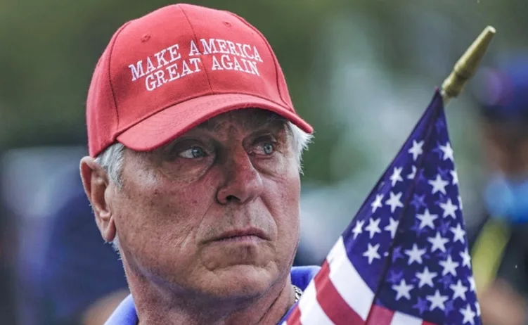 Čovjek u crvenoj kapi s natpisom "Make America Great Again" i drži malu američku zastavu.
