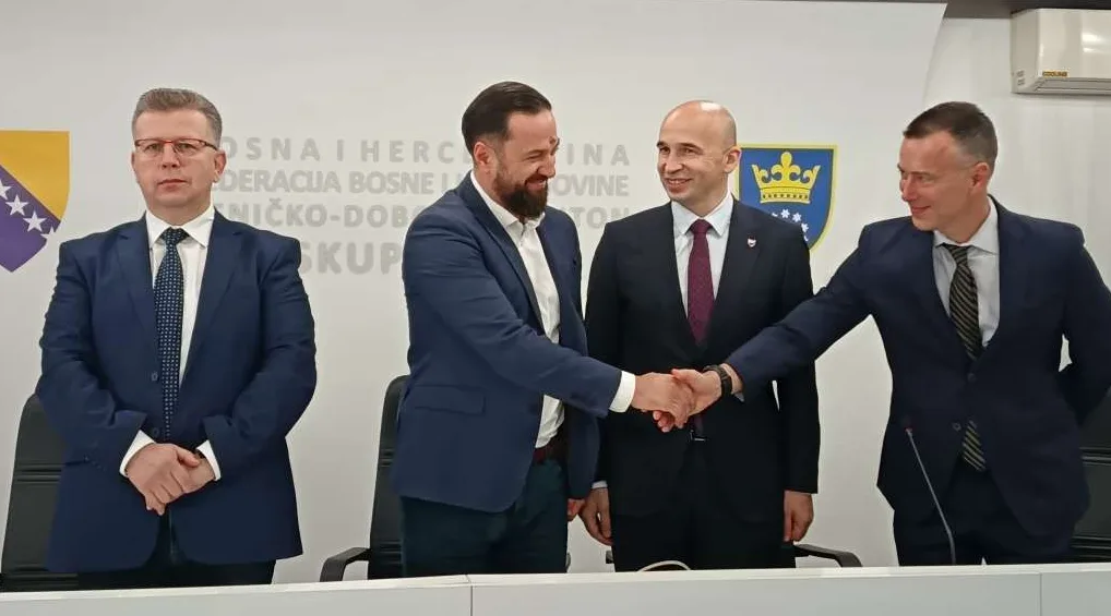 Četiri muškarca u odijelima rukuju se ispred grba Kantona Sarajevo i zastave Bosne i Hercegovine.