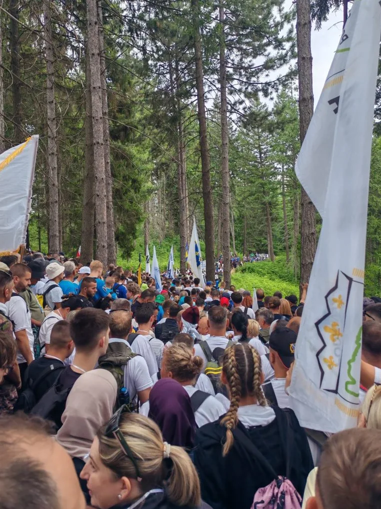 Velika grupa ljudi u povorci kroz šumu, noseći zastave.