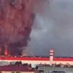 Veliki požar sa gustim crnim dimom iznad industrijskog objekta sa crvenim krovom.