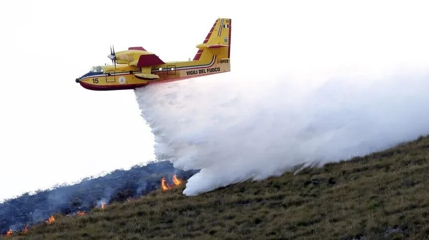 Žuti pozarni avion Canadair CL-415 izbacuje vodu na nisko rastinje zahvaćeno vatrom na padini.