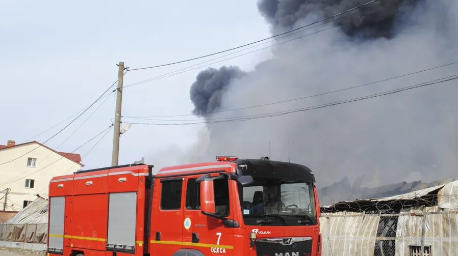 Crveni pozarni kamion s uključenim rotacijskim svjetlima parkiran ispred objekta koji gori i dimi se u Odesi.