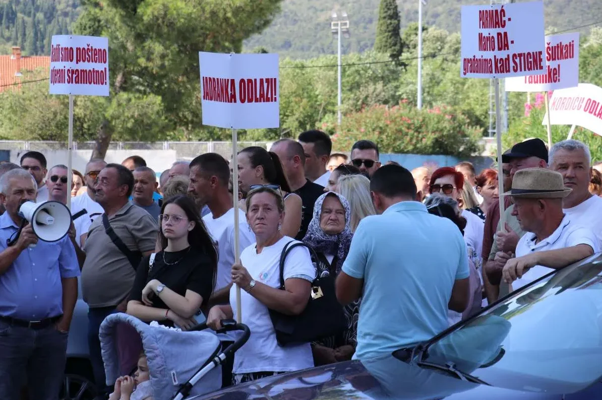 Grupa ljudi drži transparente na skupu na otvorenom.