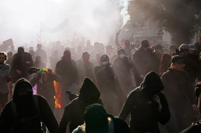 Grupa ljudi na protestu, sa dimom i bakljom koja gori u pozadini.