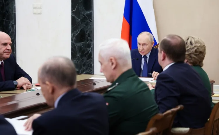 Vladimir Putin razgovara sa grupom zvaničnika za stolom, uz rusku zastavu u pozadini.