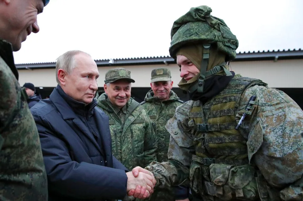 Vladimir Putin rukuje se sa ruskim vojnikom u vojnoj uniformi i kacigi.