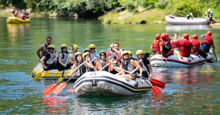 Grupa ljudi vesla u gumeni čamac na rijeci, uživajući u raftingu.