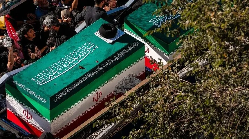 Ukrašeni kovčezi sa motivima iranske zastave i arapskim natpisima, okruženi ljudima tokom ceremonije.