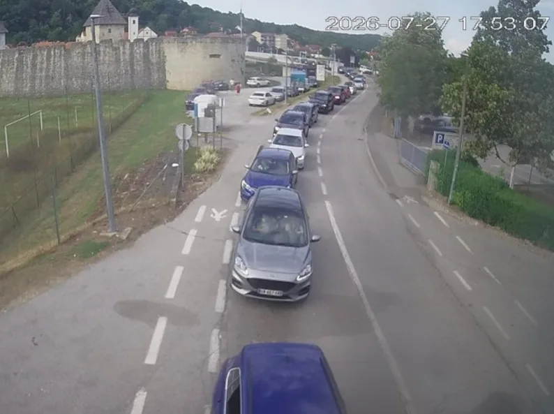 Kolona automobila na cesti ispred stare kamene tvrđave.