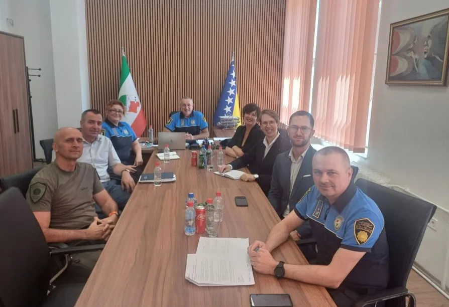Grupa policijskih službenika i civila sjedi za stolom tokom sastanka.