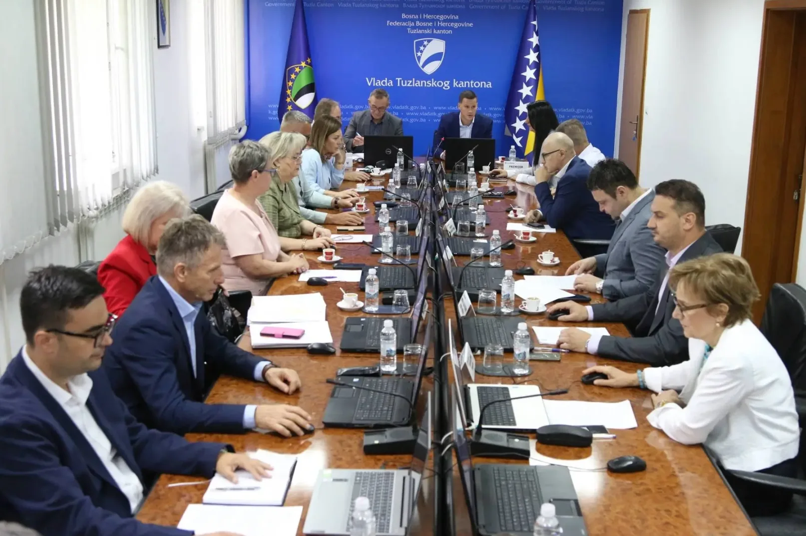 Sastanak u Vladi Tuzlanskog kantona sa prisutnim zvaničnicima i službenicima, sa laptopima i papirima na stolu.