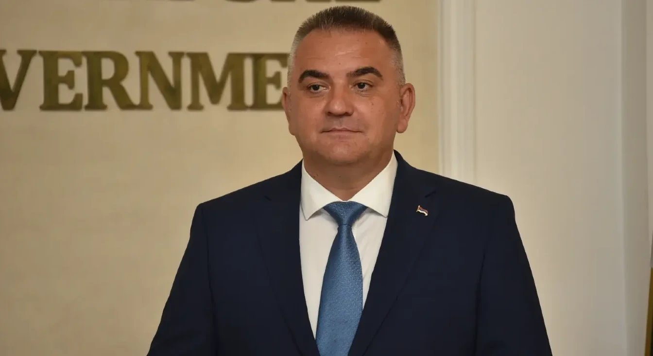 Srpski ministar u tamnom odijelu i plavoj kravati, sa zastavom Srbije na reveru.