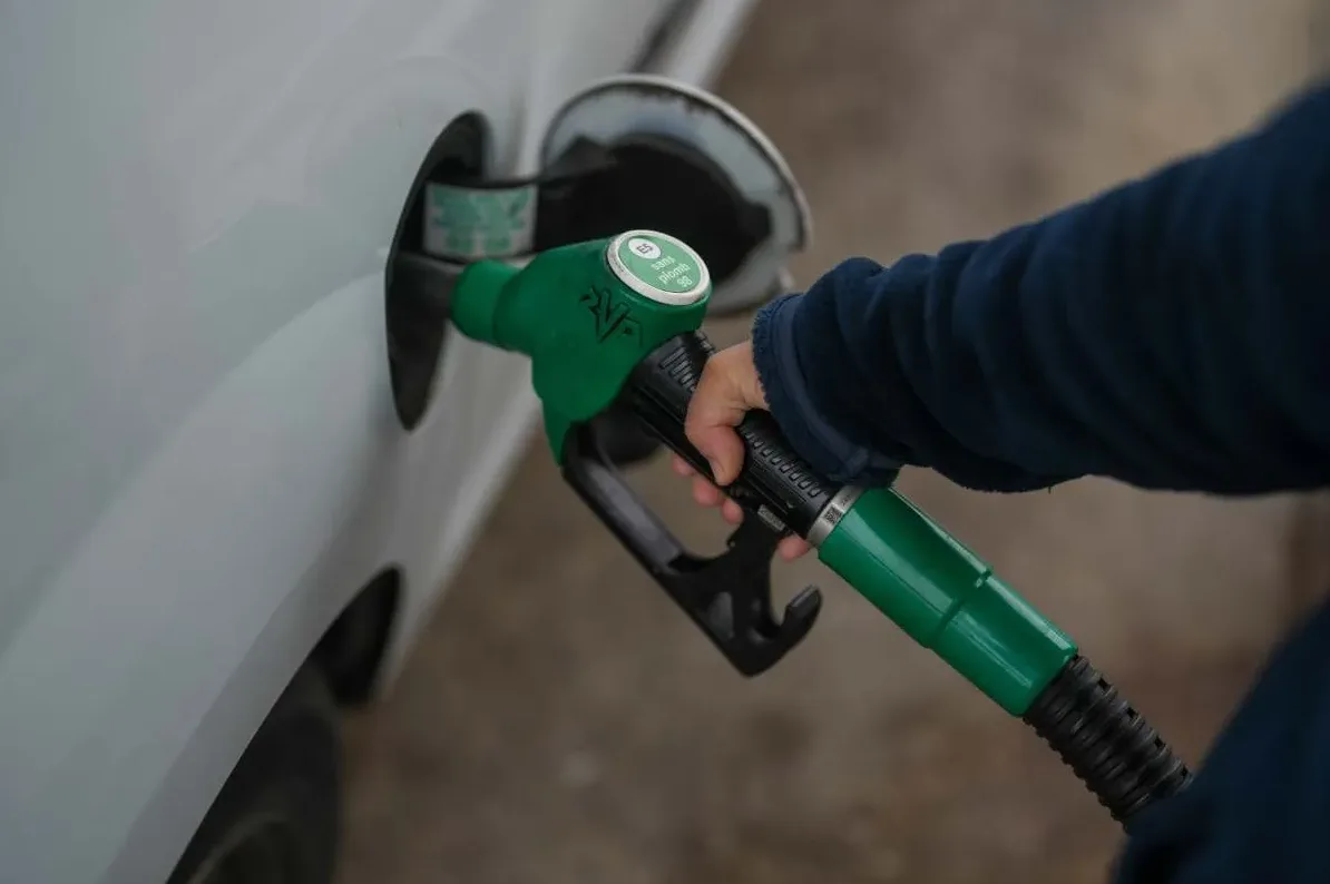 Ruka drži zelenu mlaznicu za gorivo dok sipaju benzin u rezervoar bijelog automobila.