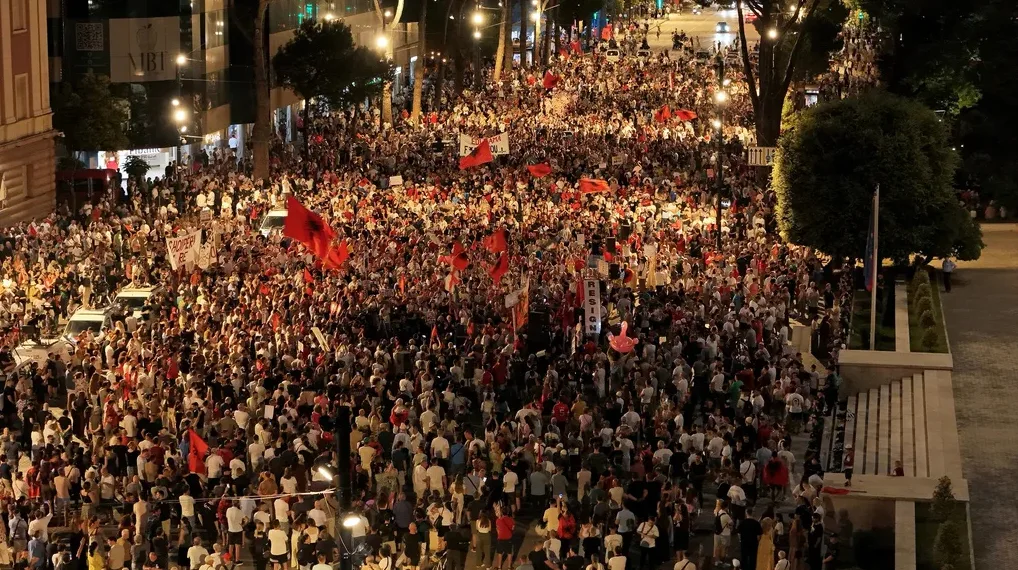 Veliki skup ljudi noću na ulici, mnogi nose crvene zastave sa dvoglavim orlom, simbolom Albanije.