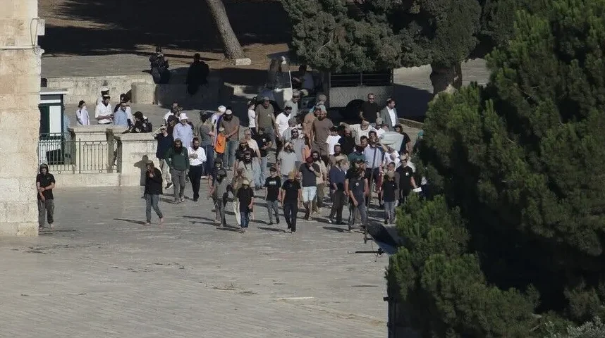 Skupina ljudi šeta po sunčanom trgu u Jerusalimu, u blizini drevne kamene građevine.
