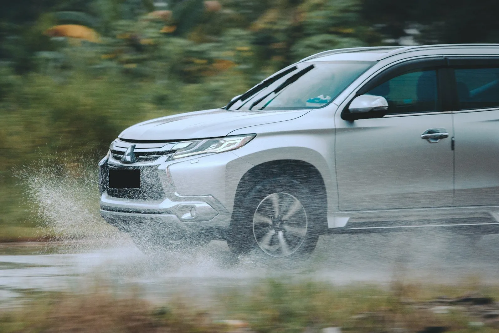 Srebrni Mitsubishi SUV prolazi kroz vodenu prepreku, podižući mnogo vode.