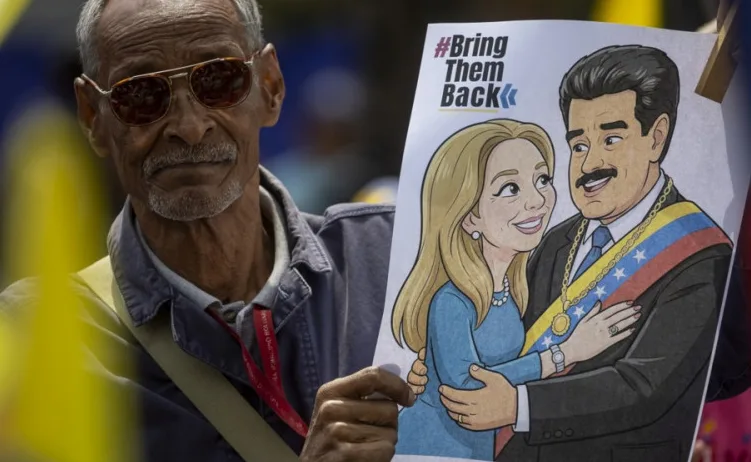Detalj fotografije prikazuje starijeg muškarca sa naočalama kako drži poster. Na posteru je karikaturalno prikazan muškarac i žena, a iznad njih natpis "#Bring Them Back".