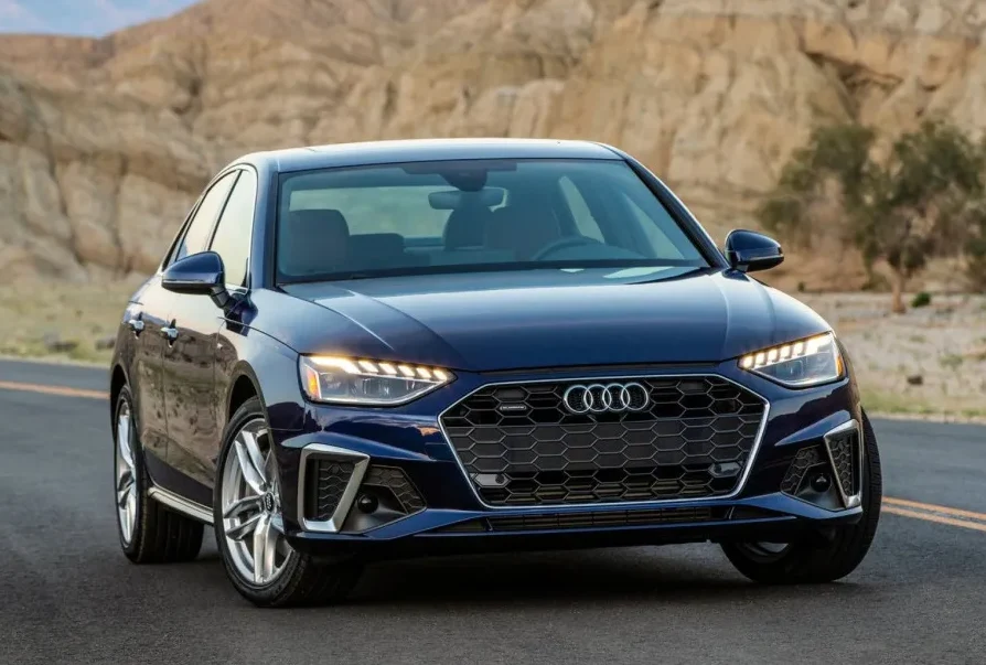 Prednji pogled na tamno plavi Audi A4 sedan parkiran na putu sa planinskim krajolikom u pozadini.