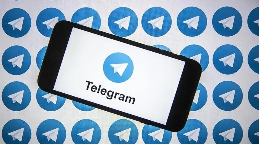 Zaslon pametnog telefona s logotipom i natpisom "Telegram". U pozadini se nalaze brojne plave kružne ikone aplikacije Telegram.
