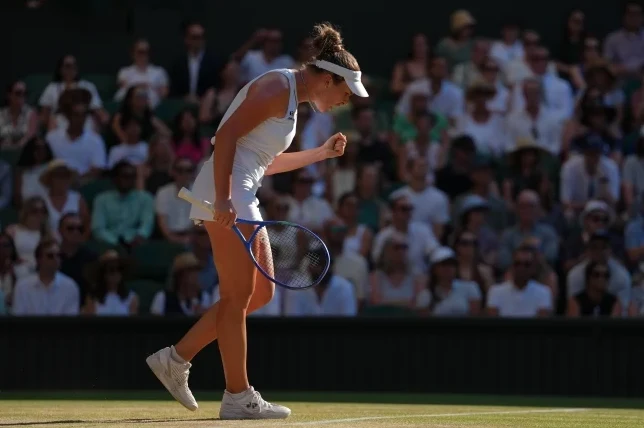 Teniserka u bijeloj opremi sa reketom u ruci, podignute pesnice i izraza ushićenja na licu, tokom meča na Wimbledonu, sa publikom u pozadini.