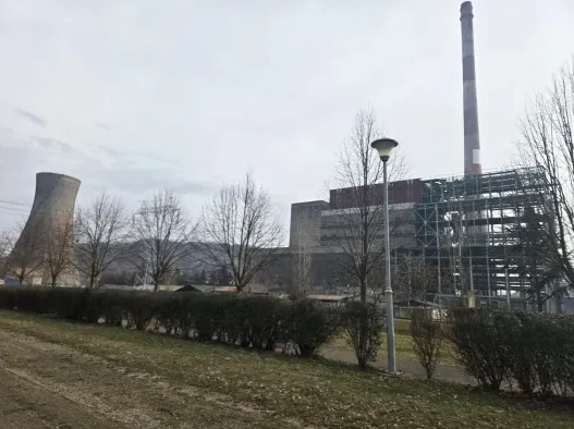 Termoelektrana s visokim dimnjakom i betonskom hladnjačom u pozadini, okružena drvećem i niskim rastinjem.