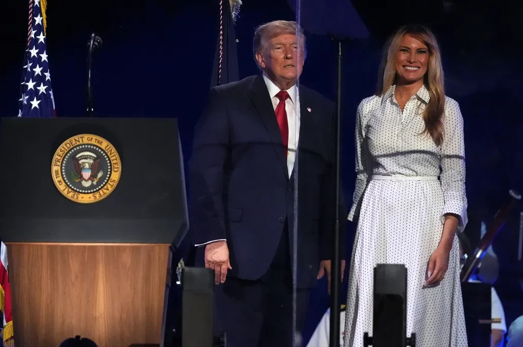 Donald Trump i Melania Trump stoje na bini pored govornice sa predsjedničkim pečatom Sjedinjenih Država.