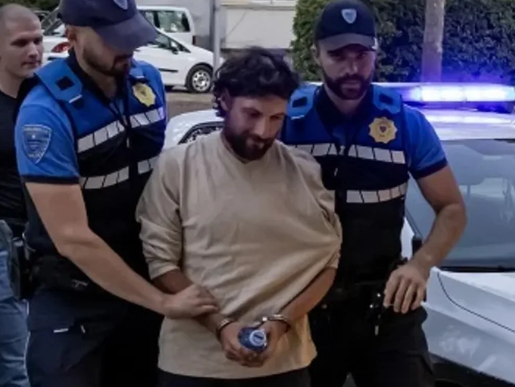 Dva policajca u plavim uniformama i prslucima vode uhapšenog muškarca u lisicama