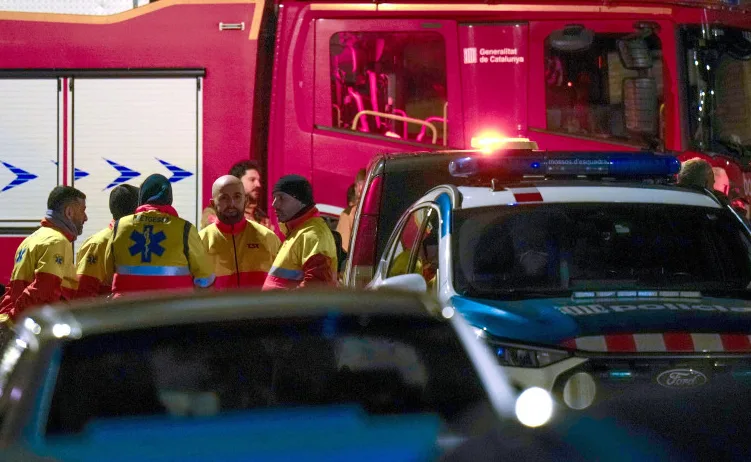 Grupa medicinara u žutim prslucima sa oznakom hitne pomoći okupljena ispred vatrogasnog vozila Generalitat de Catalunya. U prvom planu se nazire policijsko vozilo sa uključenim rotacijskim svjetlima.