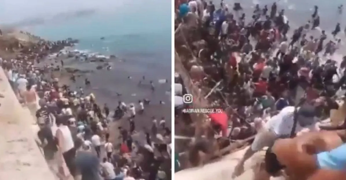 Velika grupa ljudi na obali mora, neki u vodi, pokušavaju se ukrcati ili se spašavaju.