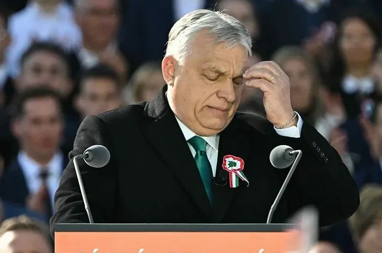 Viktor Orban dodiruje svoje čelo dok govori za govornicom.