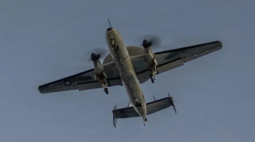 Vojni avion sa dva motora leti iznad glave, sa krilima podignutim.