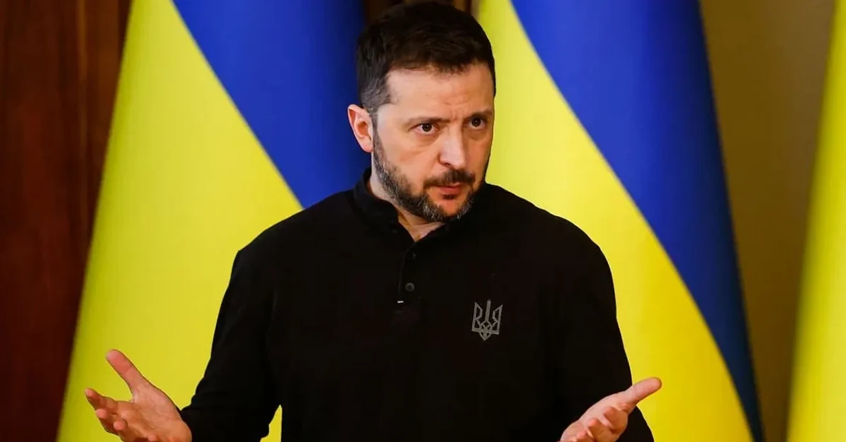 Volodimir Zelenski, ukrajinski predsjednik, nosi crnu majicu sa grbom Ukrajine, sa ukrajinskim zastavama u pozadini.