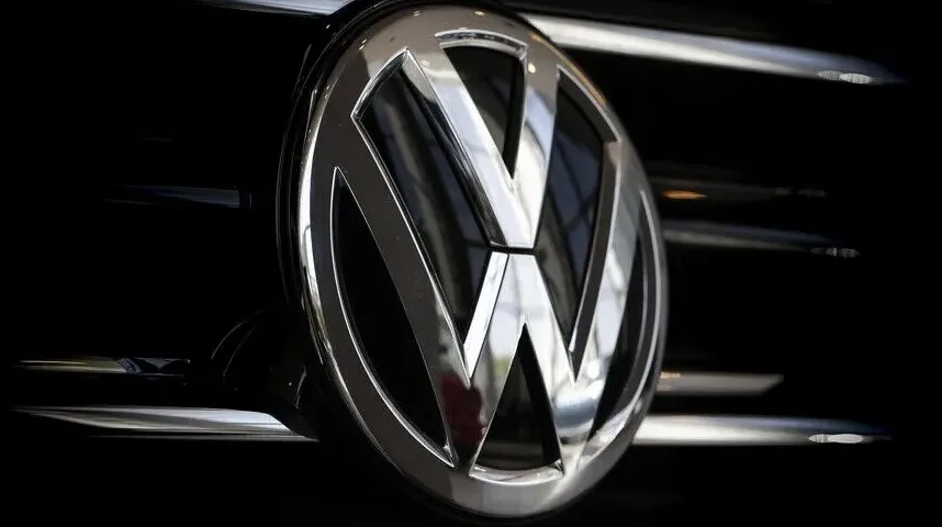 Detaljan prikaz hromiranog Volkswagenovog znaka na crnoj rešetki hladnjaka automobila.