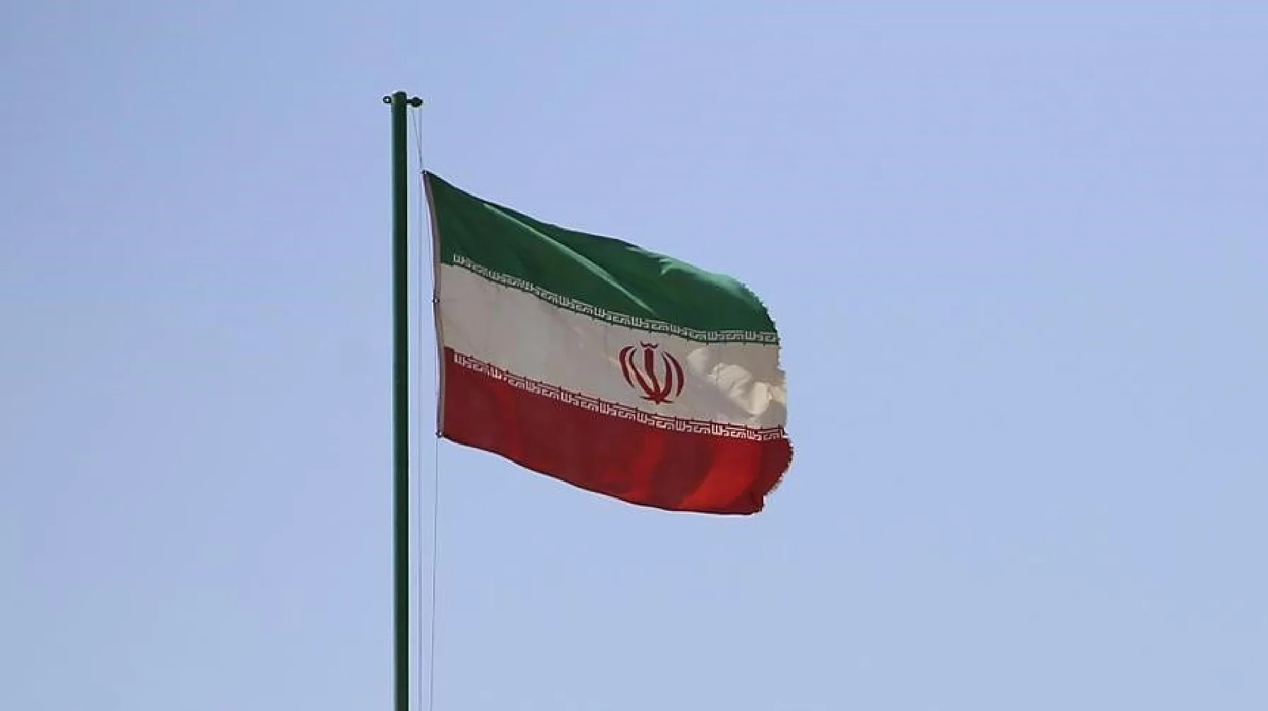 Zastava Islamske Republike Iran leprša na zelenom jarbolu protiv vedrog neba.