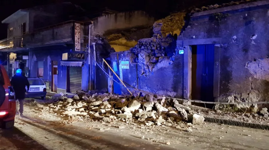 Fotografija prikazuje ulicu noću s razrušenom zgradom i šutom na kolovozu.